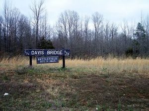 photo shows a large wooden sign with white text that reads "davis battlefield" the sign is in front of a field with tall grasses
